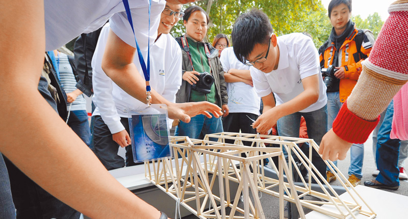 几名土木工程系大学生,摆放用细木条制作的桥梁结构模型,准备进行承重