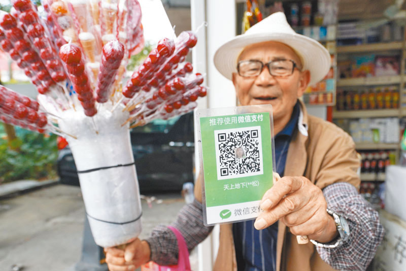 深圳街头一位卖糖葫芦的商贩向顾客出示移动支付二维码,方便顾客扫码