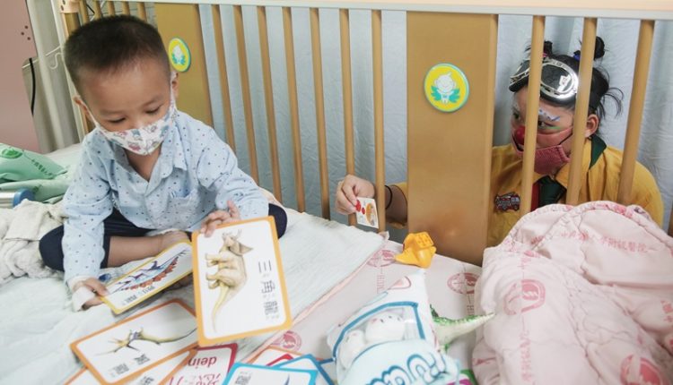 隔著病床的柵欄，小丑醫生朱怡文遞出了象徵友誼的名片給正在排列動物卡片，對她愛理不理的病童。（季志翔攝）