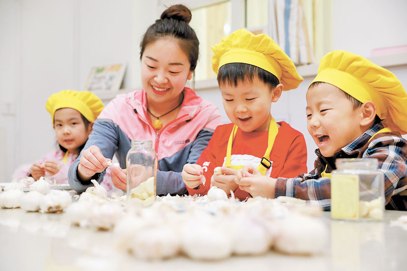1月11日,在河北石家莊市第一幼兒園,老師和孩子們在剝蒜準備腌制臘八蒜。(新華社)
