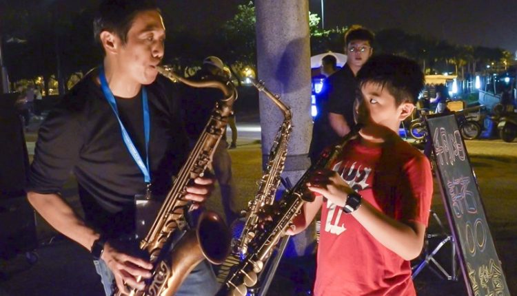 台南音樂工作者曾進興(左)為最小的兒子曾璟文示範薩克斯風吹奏技巧，他三個孩子從小耳濡目染，個個都會演奏多種樂器。（黃子明攝）