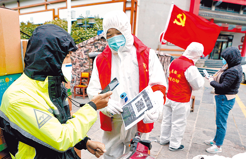 4月11日,疫情防控人員在武漢一小區封控點,對進出小區的人員掃描健康碼。(新華社)
