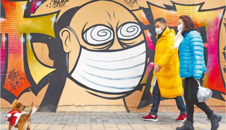 上海市民戴著口罩在街頭散步，經過口罩主題的塗鴉牆。（中新社資料照片）