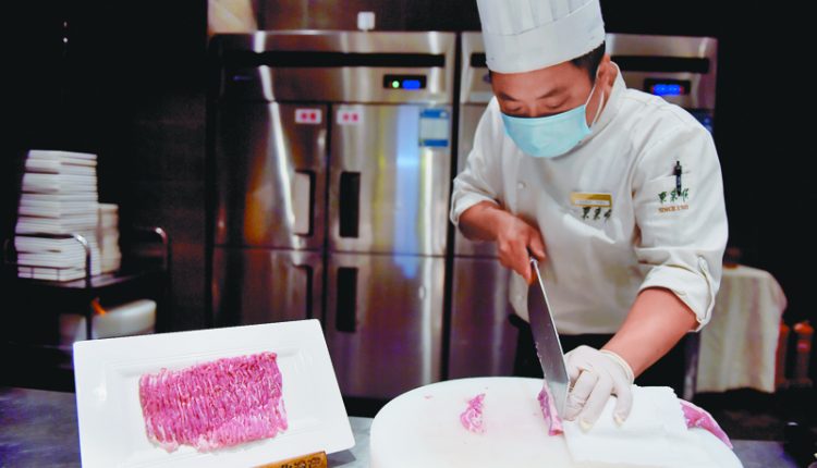 6月14日，北京一家餐廳廚房內，廚師在切羊肉。（新華社）
